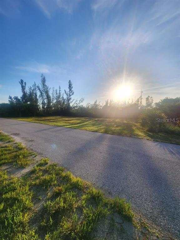 A paved road runs alongside a grassy, sunlit vacant lot with trees in the background — 6146 LANDINGS WAY, PUNTA GORDA, FL