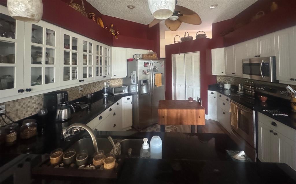 A kitchen features white cabinets, black countertops, stainless steel appliances, and dark red walls — 4062 WESTBOURNE CIRCLE, SARASOTA, FL