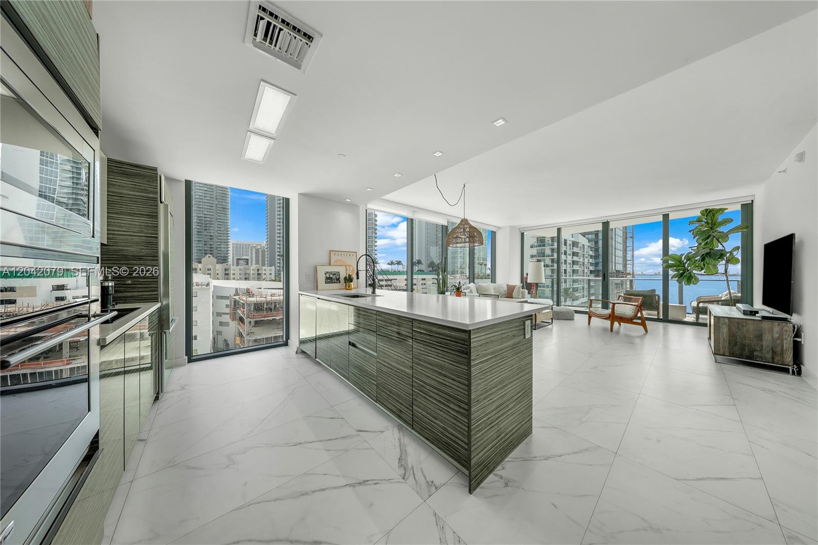 A modern kitchen and living area with a large island, marble floors, and floor-to-ceiling windows — 460 NE 28th St # 701, Miami FL 33137, MIAMI, FL