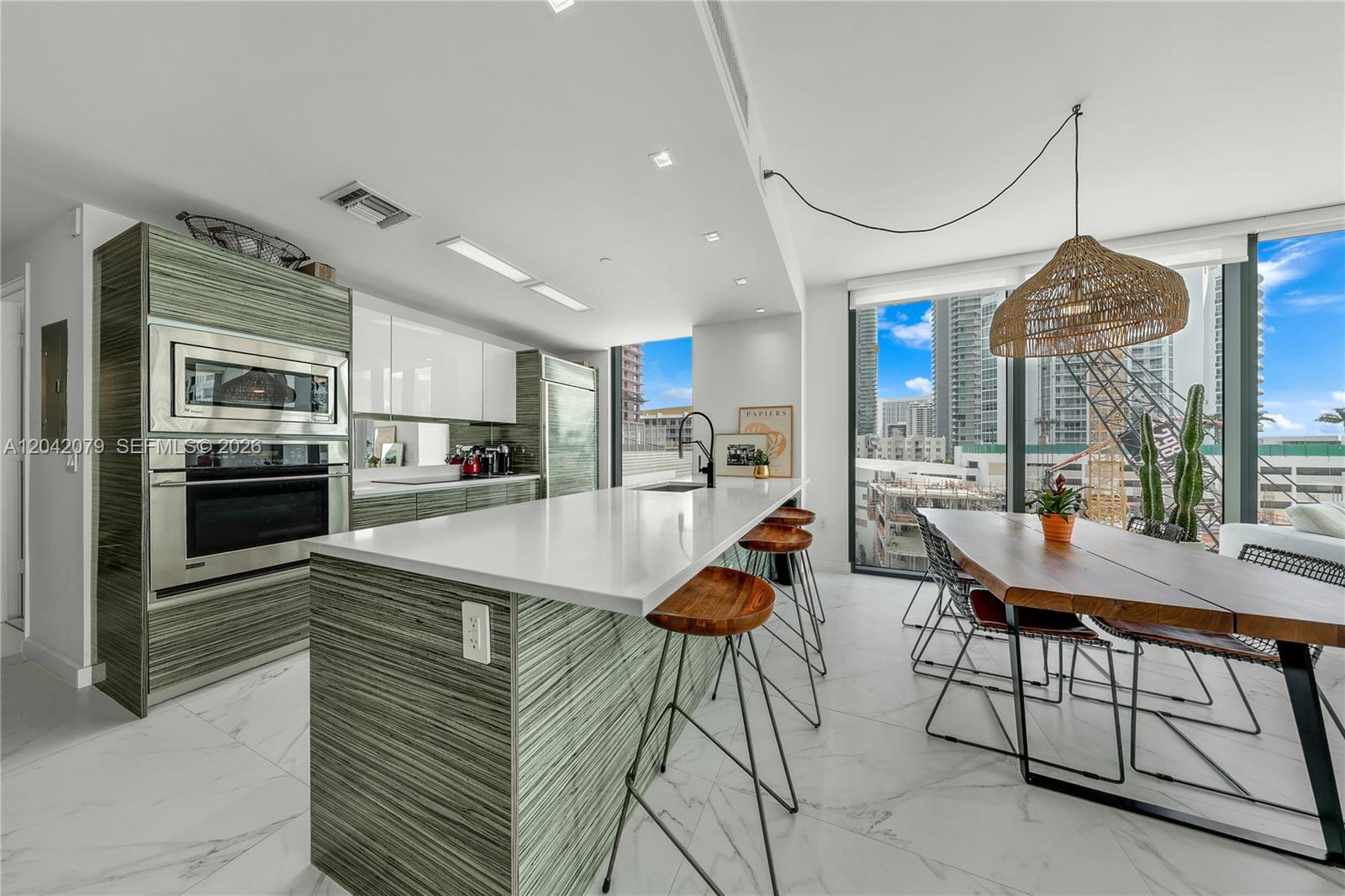 A modern kitchen features a white island, wood-grain cabinetry, and a dining area with city views — 460 NE 28th St # 701, Miami FL 33137, MIAMI, FL