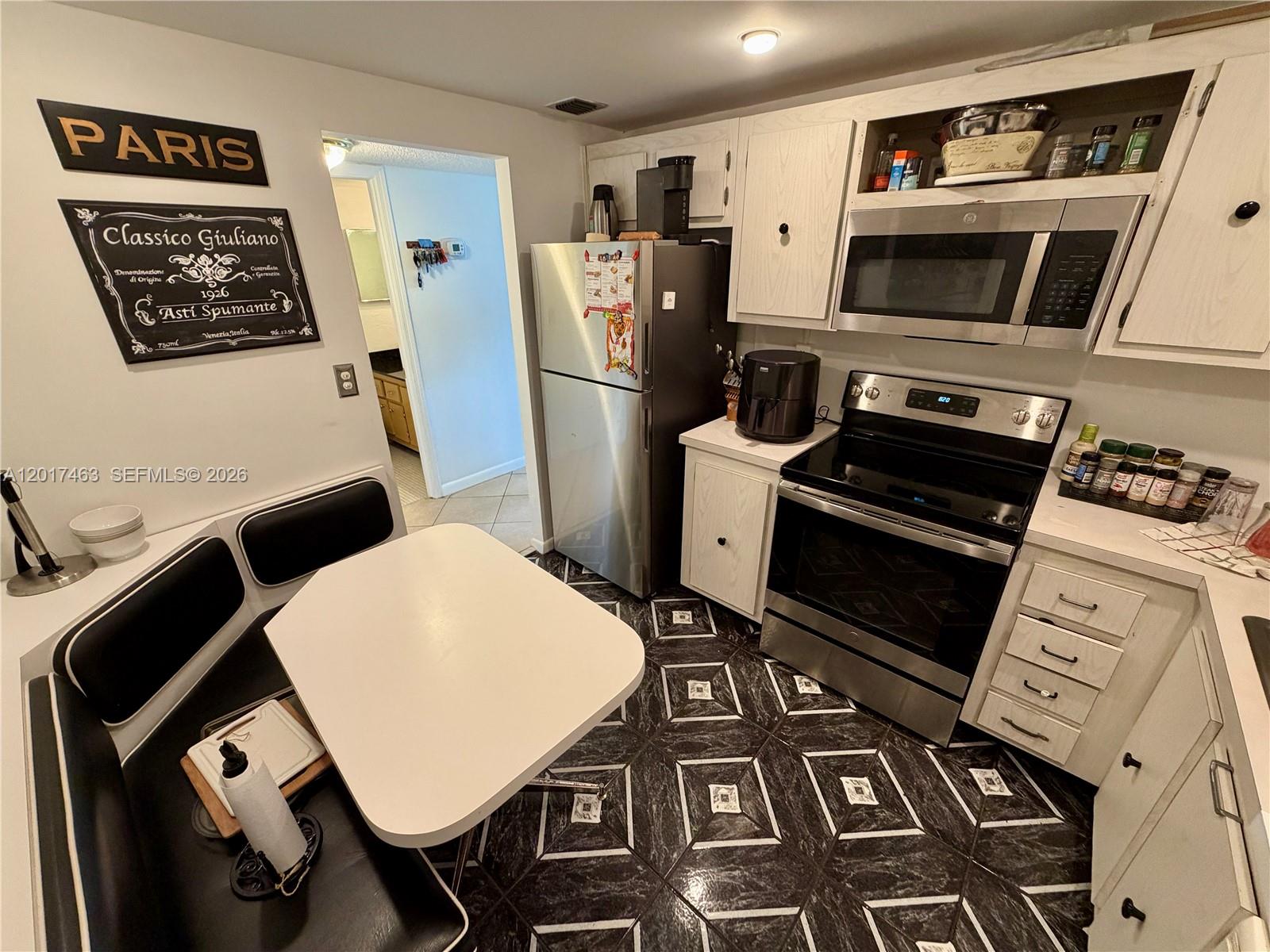 A kitchen features white cabinets, stainless steel appliances, a dining nook, and patterned black flooring — 3800 S Ocean Dr # 1208, Hollywood FL 33019, HOLLYWOOD, FL