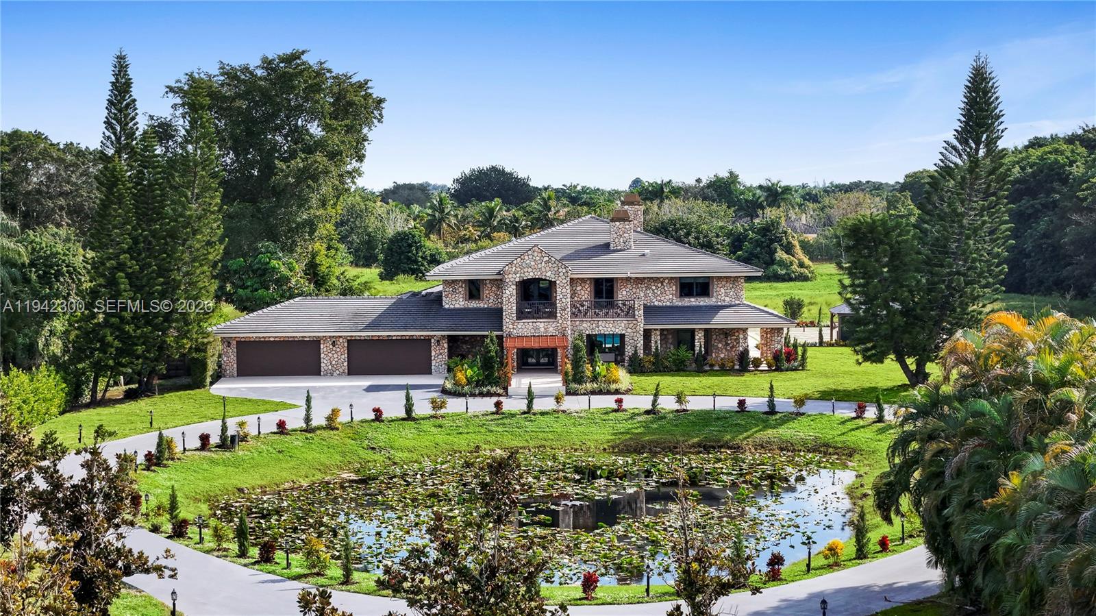 A stone-clad two-story house sits behind a lily pad pond and a circular driveway — 3320 SW 121st Ave, Davie FL 33330, DAVIE, FL