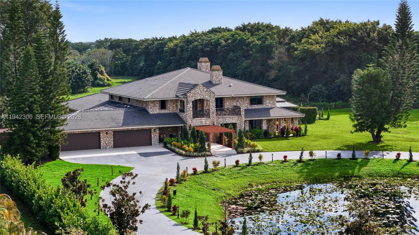 A large two-story stone house with a multi-car garage sits beside a lily-covered pond — 3320 SW 121st Ave, Davie FL 33330, DAVIE, FL