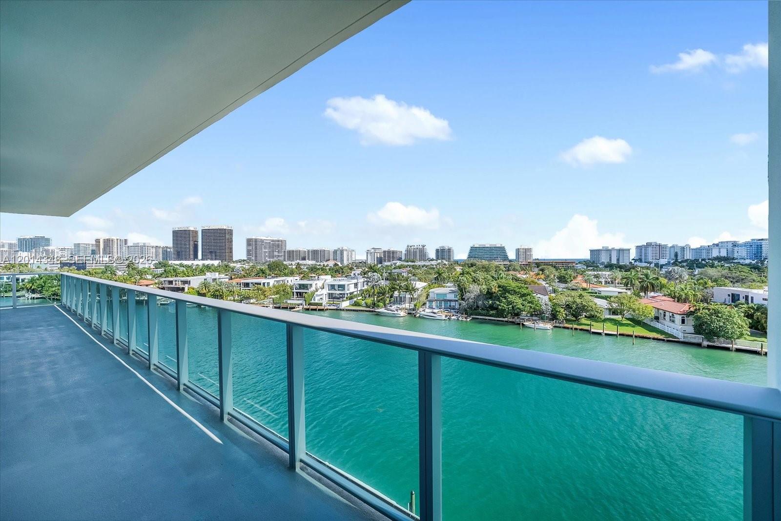 A high-rise balcony with a glass railing overlooks a canal and a coastal city skyline — 9201 E Bay Harbor, Bay Harbor Islands FL 33154, BAY HARBOR ISLANDS, FL