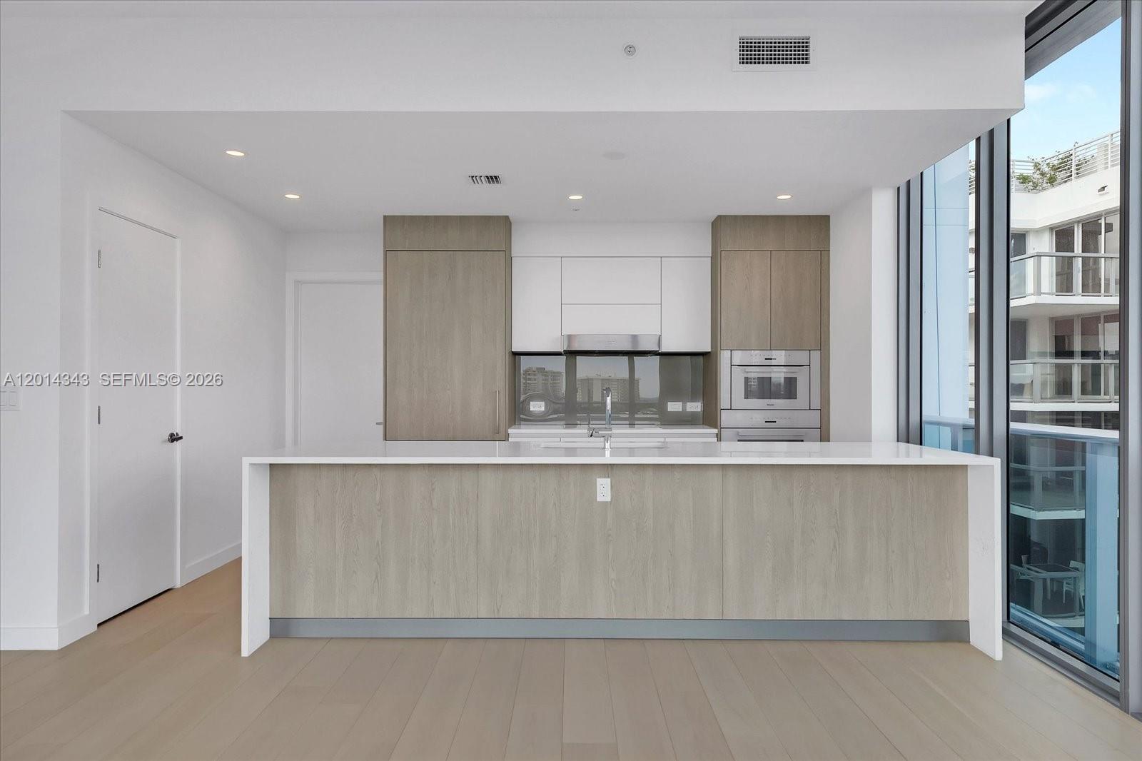 A modern kitchen features light wood cabinetry, white countertops, and a large central island — 9201 E Bay Harbor, Bay Harbor Islands FL 33154, BAY HARBOR ISLANDS, FL