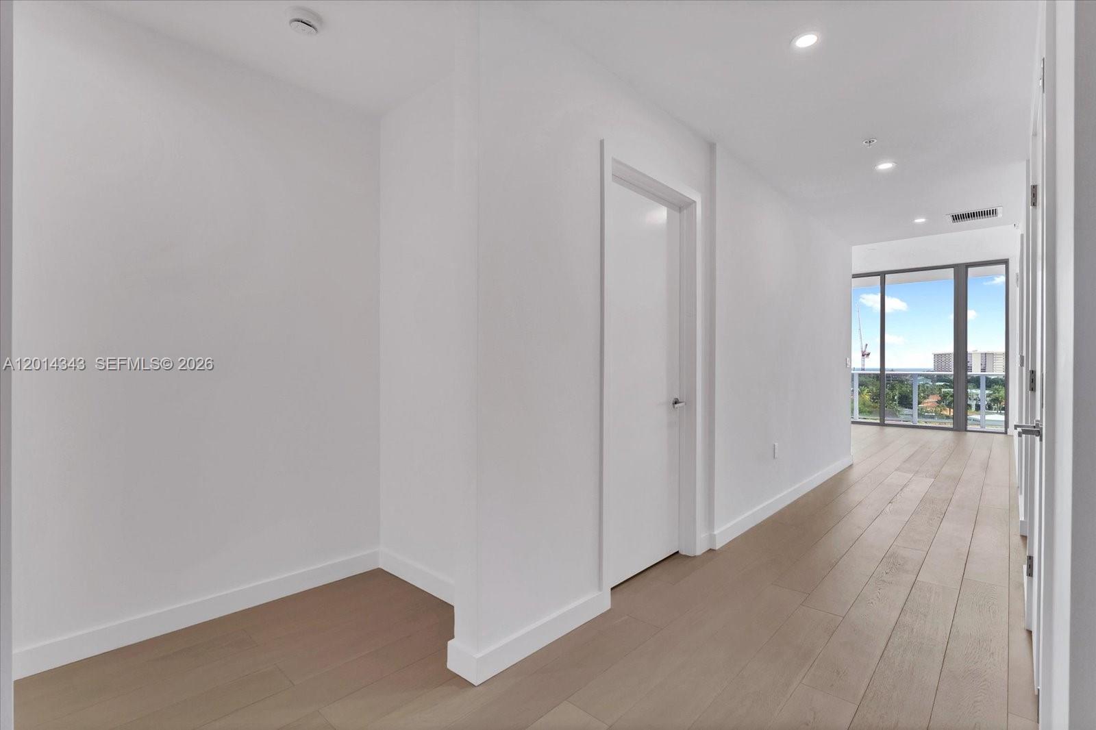 A bright hallway with light wood flooring leads toward a room with floor-to-ceiling windows — 9201 E Bay Harbor, Bay Harbor Islands FL 33154, BAY HARBOR ISLANDS, FL