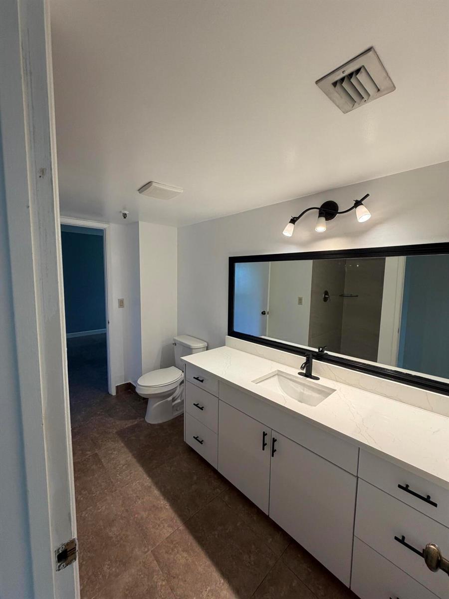 A bathroom features a white vanity with a black-framed mirror and a toilet — 2202 S Cypress Bend Drive # 101, Pompano Beach FL 33069, POMPANO BEACH, FL
