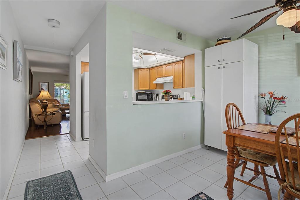 A dining area with tile floors looks through a pass-through window into a wood-cabinet kitchen — 28201 PINE HAVEN WAY UNIT 145, BONITA SPRINGS, FL