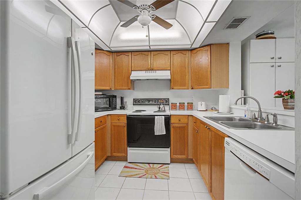 A kitchen with wood cabinets, white appliances, a double sink, and a tray ceiling — 28201 PINE HAVEN WAY UNIT 145, BONITA SPRINGS, FL