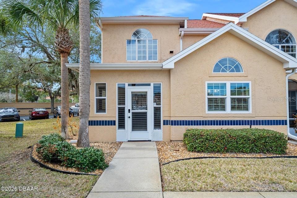 The exterior of a two-story tan stucco townhouse features a front entrance and walkway — 25 MARINA POINT PLACE, PALM COAST, FL