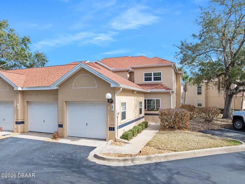 A tan two-story townhouse exterior features a white garage door and a paved walkway — 25 MARINA POINT PLACE, PALM COAST, FL