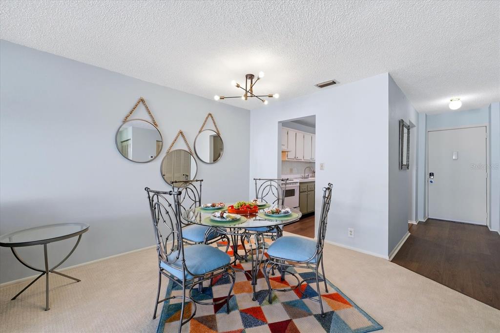 A dining area features a glass table, four blue chairs, a colorful rug, and wall mirrors — 2060 MARILYN STREET UNIT 211, CLEARWATER, FL