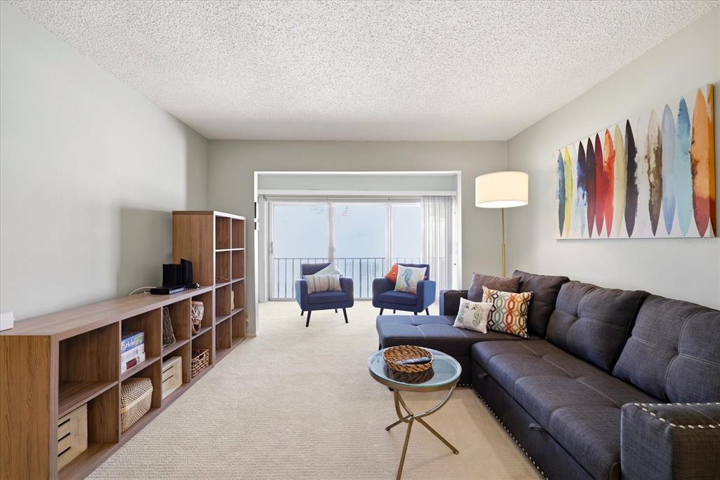 A living room features a grey sectional sofa, a wooden bookshelf, and two blue armchairs — 2060 MARILYN STREET UNIT 211, CLEARWATER, FL