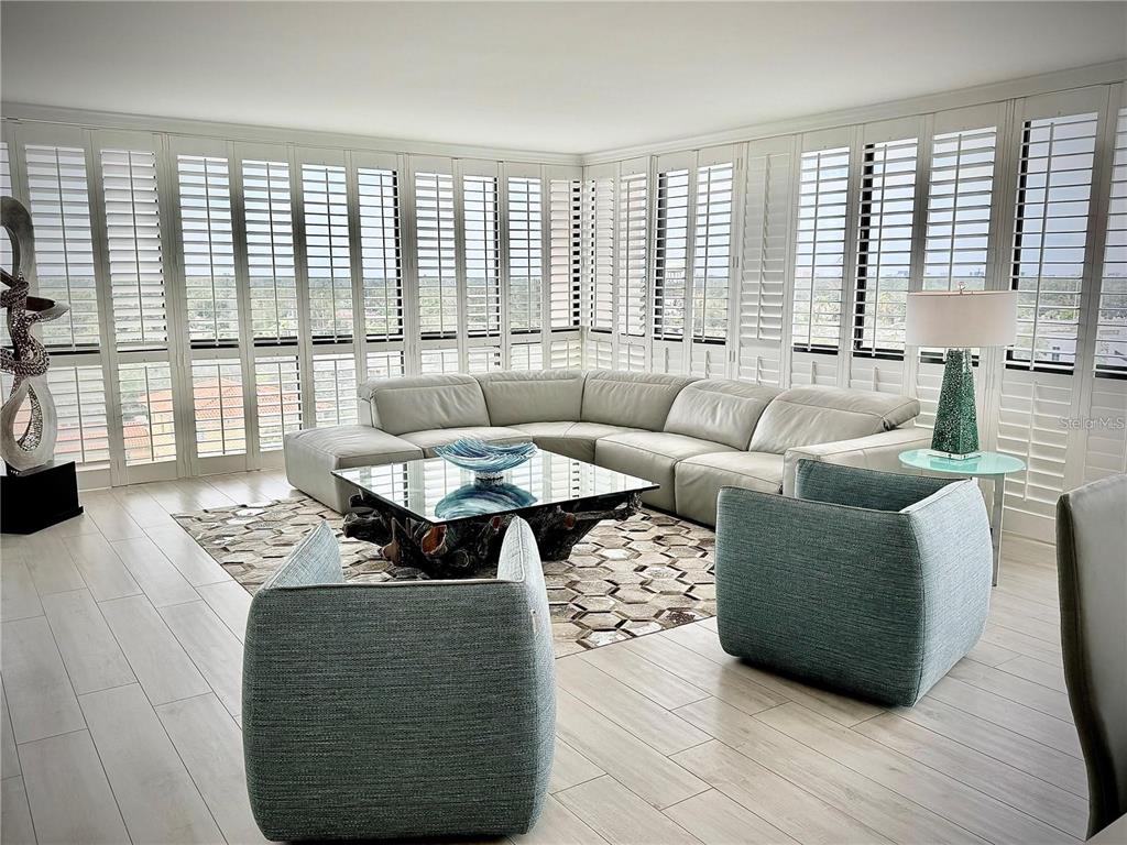 A living room features a large sectional sofa, two blue armchairs, and floor-to-ceiling shutters — 3301 BAYSHORE BOULEVARD UNIT 1001E, TAMPA, FL