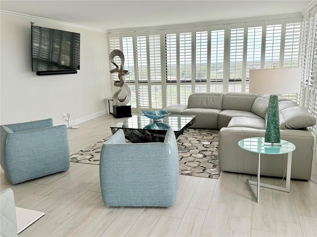 A living room features a grey sectional, two blue armchairs, and floor-to-ceiling shuttered windows — 3301 BAYSHORE BOULEVARD UNIT 1001E, TAMPA, FL