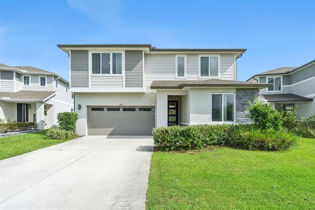 A two-story suburban house with a gray garage, light siding, and a stone accent wall — 4148 SOUTHERN VISTA LOOP, ST CLOUD, FL
