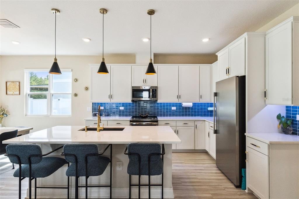 A modern kitchen features white cabinets, a blue tiled backsplash, and a large quartz island — 4148 SOUTHERN VISTA LOOP, ST CLOUD, FL