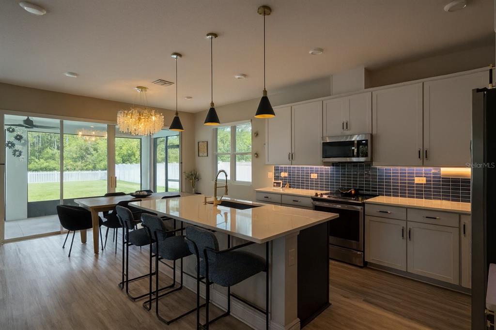 A modern kitchen features a large island with bar seating, white cabinetry, and blue backsplash — 4148 SOUTHERN VISTA LOOP, ST CLOUD, FL