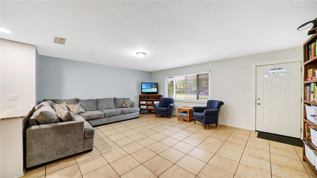 A living room features a large gray sectional sofa, two blue armchairs, and tiled flooring — 745 WILDWOOD DRIVE, ST AUGUSTINE, FL