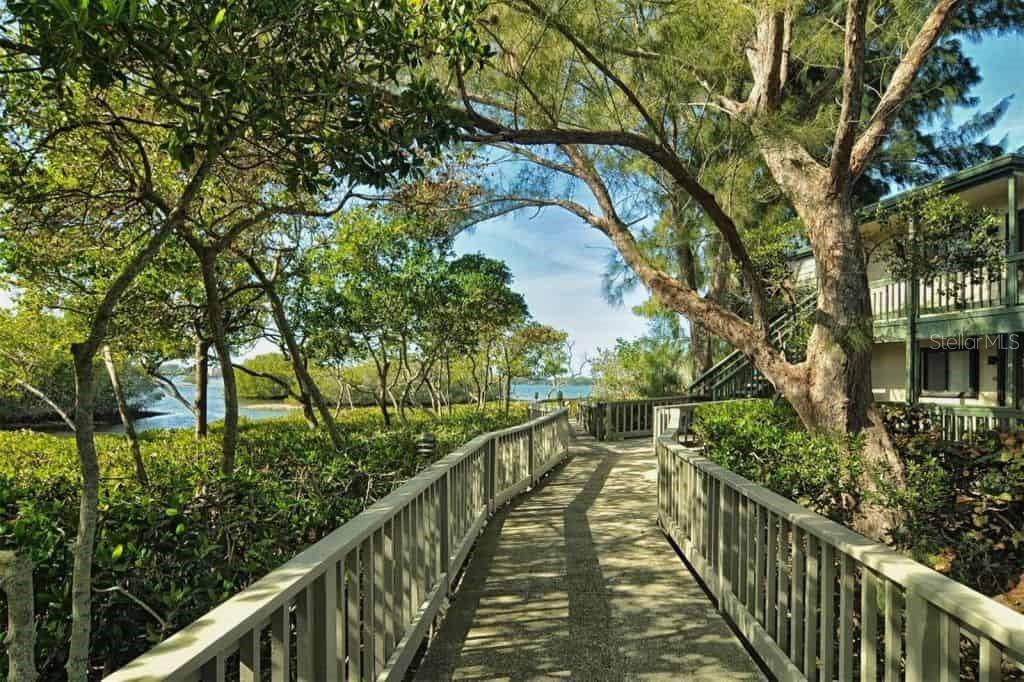 A concrete walkway with wooden railings leads through trees toward a waterfront view — 1628 CLOWER CREEK DRIVE UNIT 125, SARASOTA, FL