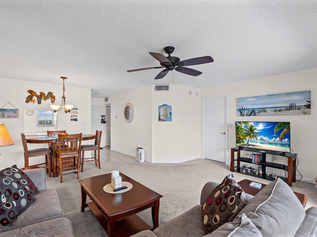 A living room and dining area feature beige carpet, a ceiling fan, and coastal decor — 6800 20TH AVENUE N UNIT 503, ST PETERSBURG, FL