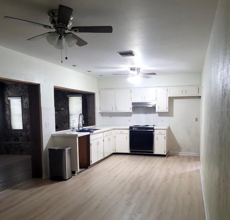 A kitchen with white cabinets, a black stove, and light wood-look flooring — 4716 W SAN RAFAEL STREET, TAMPA, FL