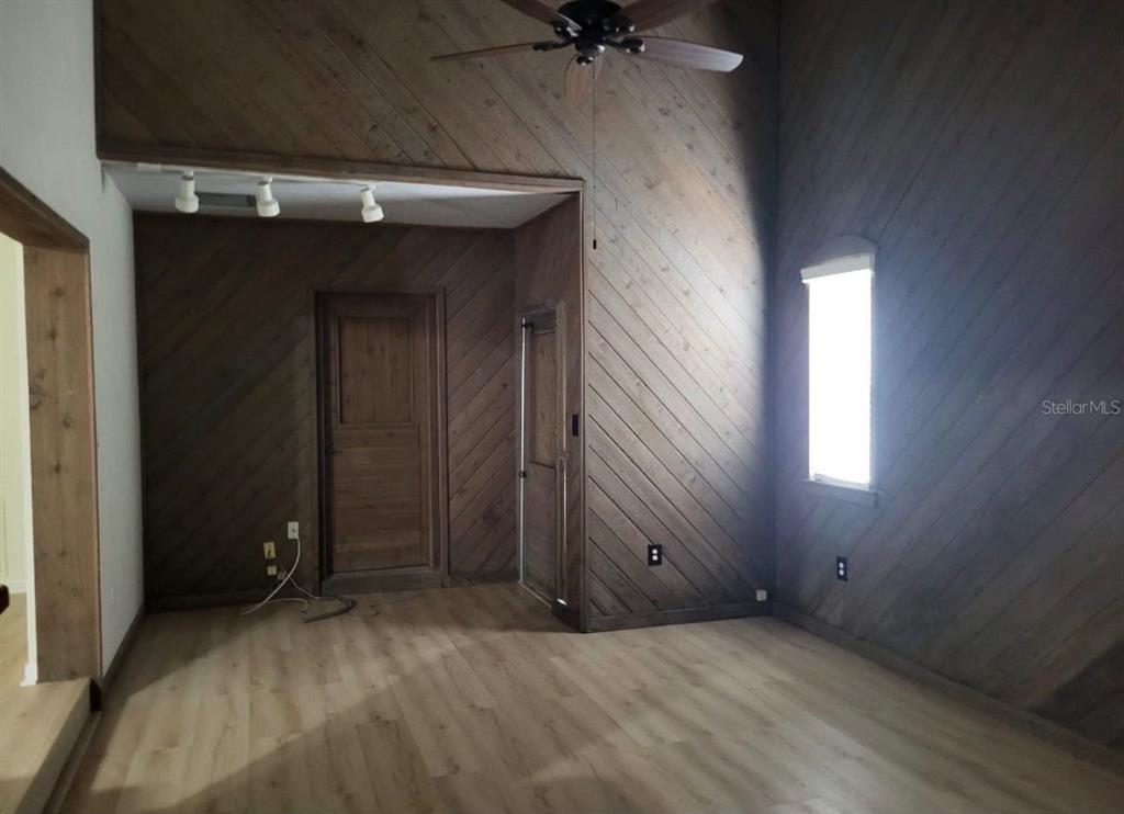 A room with diagonal wood-paneled walls, light wood flooring, a ceiling fan, and a window — 4716 W SAN RAFAEL STREET, TAMPA, FL