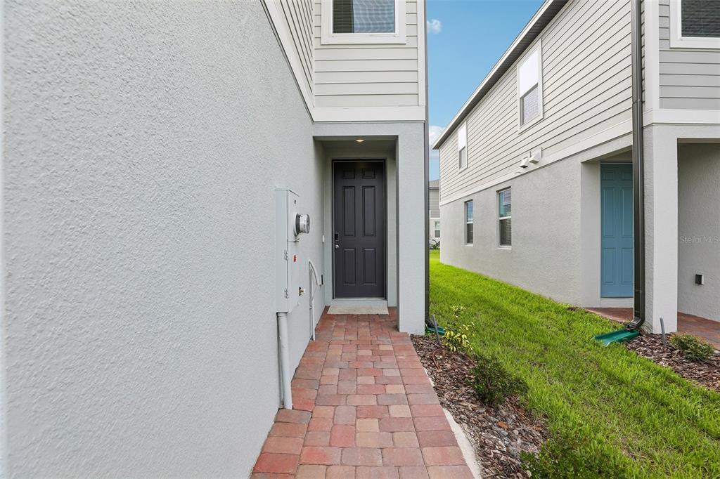 A paved walkway leads to a dark front door between two residential building exteriors — 4573 RANGELAND WAY, ST CLOUD, FL