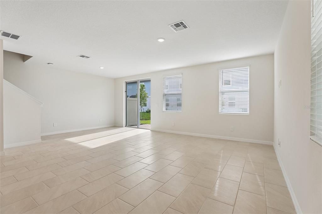 An empty living room features light-colored tile flooring, white walls, and a sliding glass door — 4573 RANGELAND WAY, ST CLOUD, FL