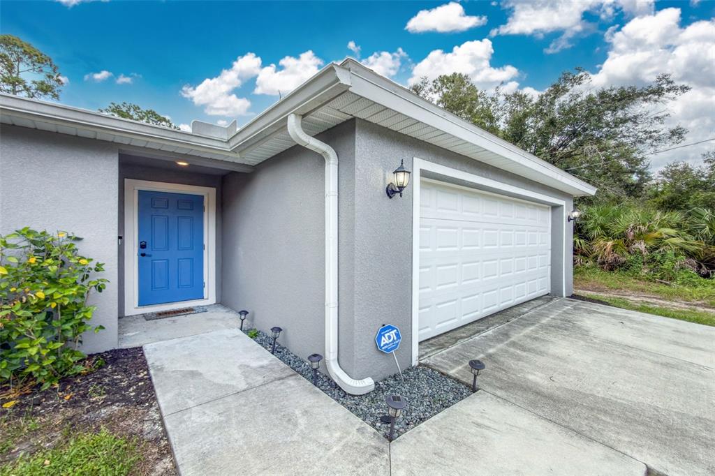 A gray house exterior features a bright blue front door and a white garage door — 18346 SAGAMORE AVENUE, PORT CHARLOTTE, FL