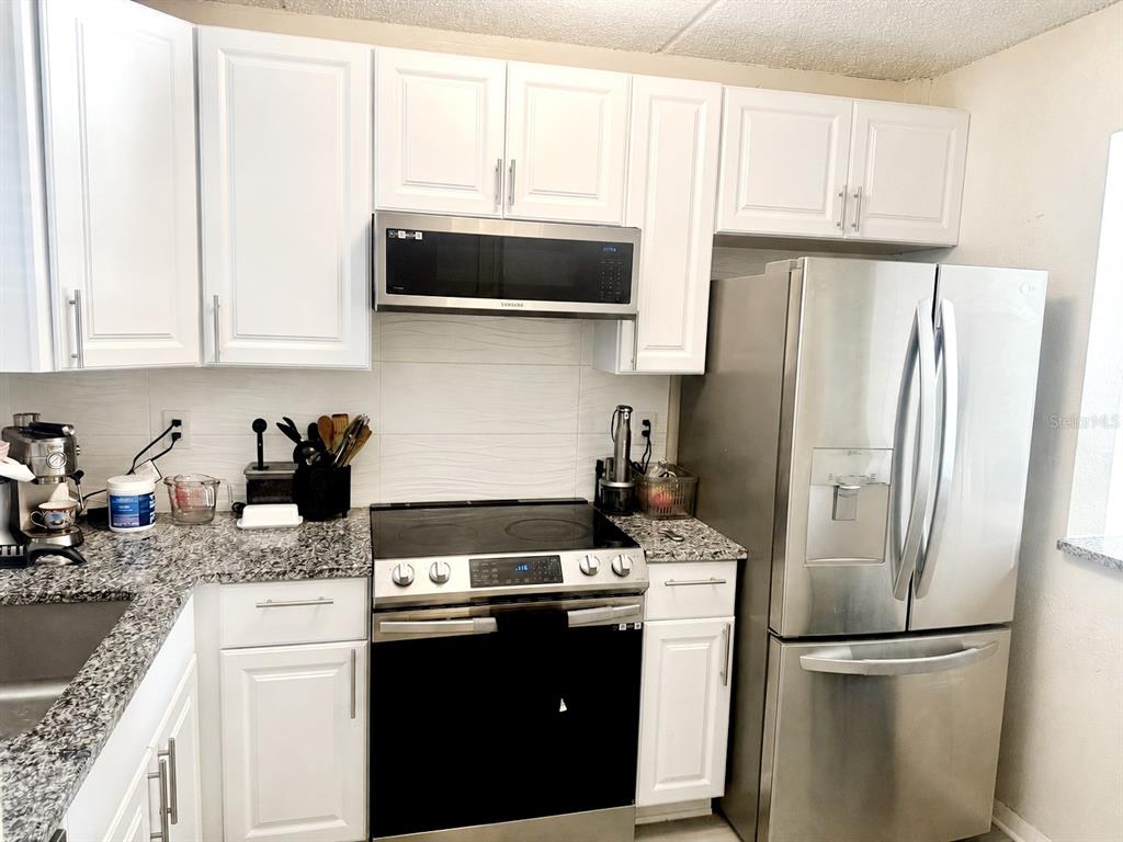 A kitchen features white cabinets, stainless steel appliances, and speckled granite countertops — 2864 SOMERSET PARK DRIVE UNIT 2864, TAMPA, FL