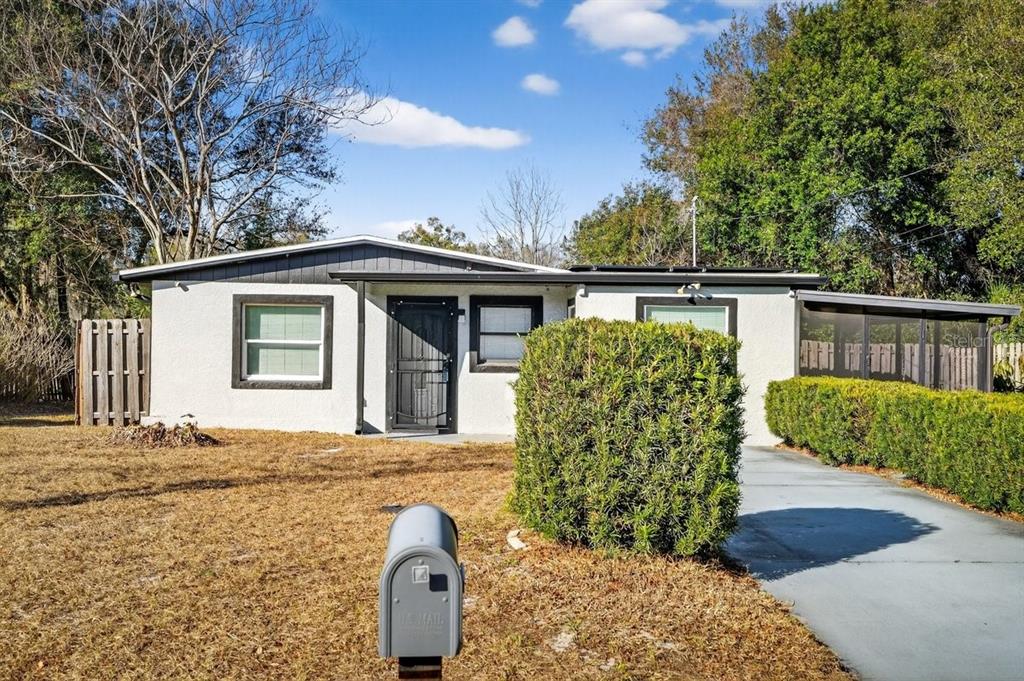 A single-story house with a white stucco exterior, a dark roof, and a paved driveway — 493 W BALTIMORE DRIVE, DELAND, FL