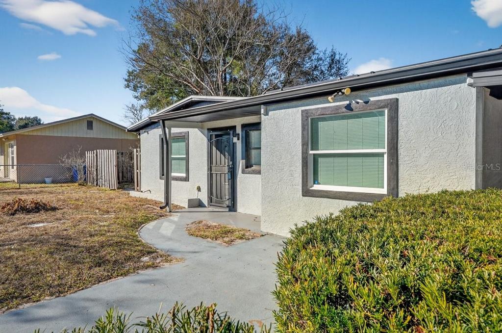A single-story house with a white stucco exterior, dark trim, and a concrete walkway — 493 W BALTIMORE DRIVE, DELAND, FL