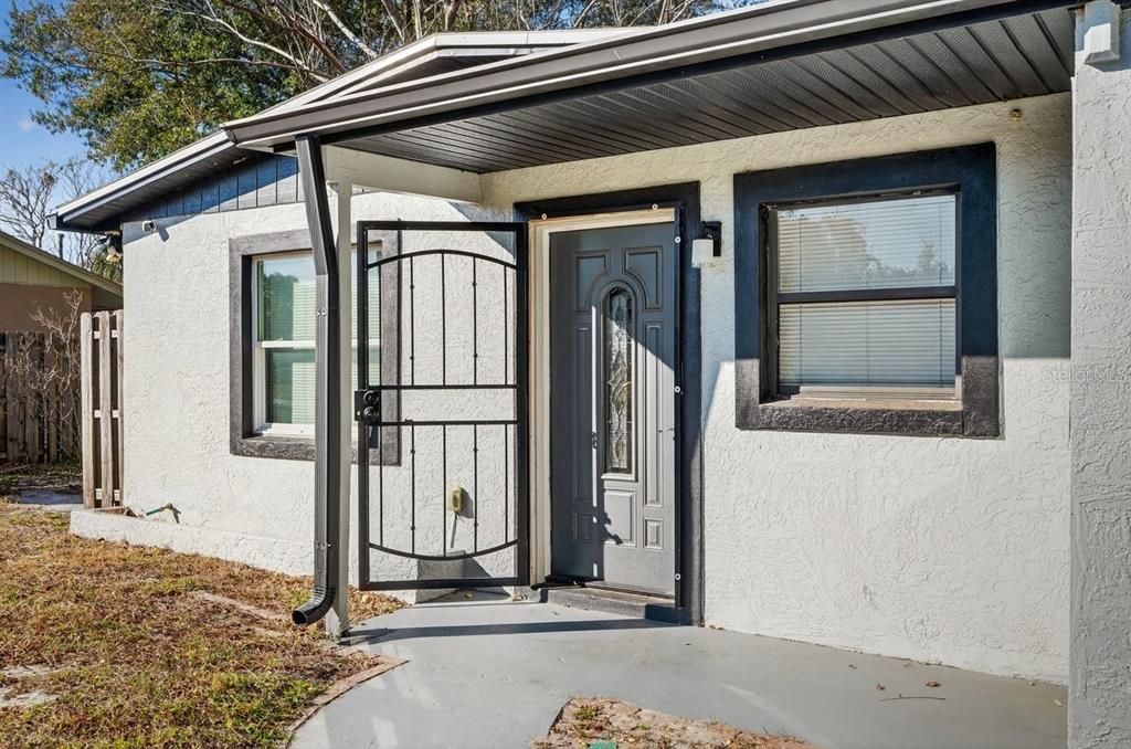 The exterior of a white stucco house features a gray front door and metal security gate — 493 W BALTIMORE DRIVE, DELAND, FL