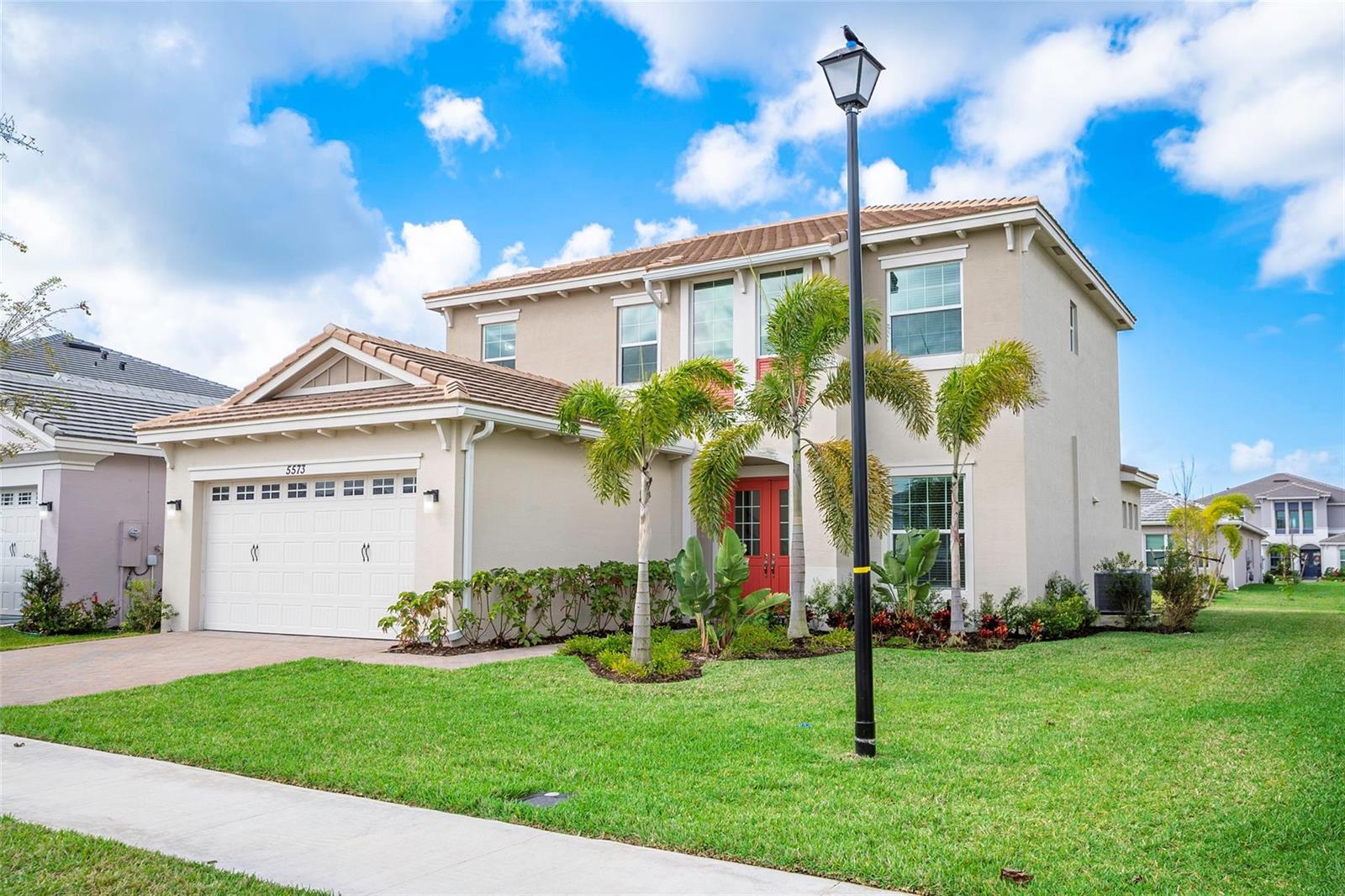 A two-story suburban house with a tan stucco exterior, red front doors, and palm trees — 5573 Zestar Lane, Westlake FL 33470, WESTLAKE, FL