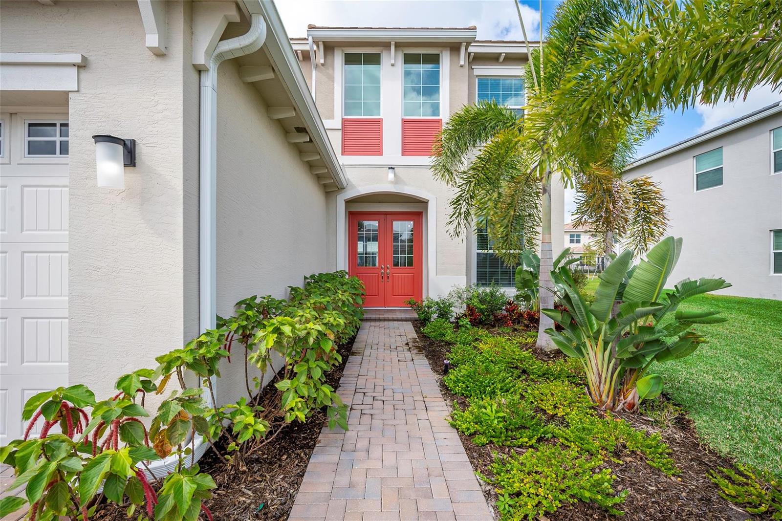 A paved walkway leads to the red double front doors of a two-story suburban home — 5573 Zestar Lane, Westlake FL 33470, WESTLAKE, FL