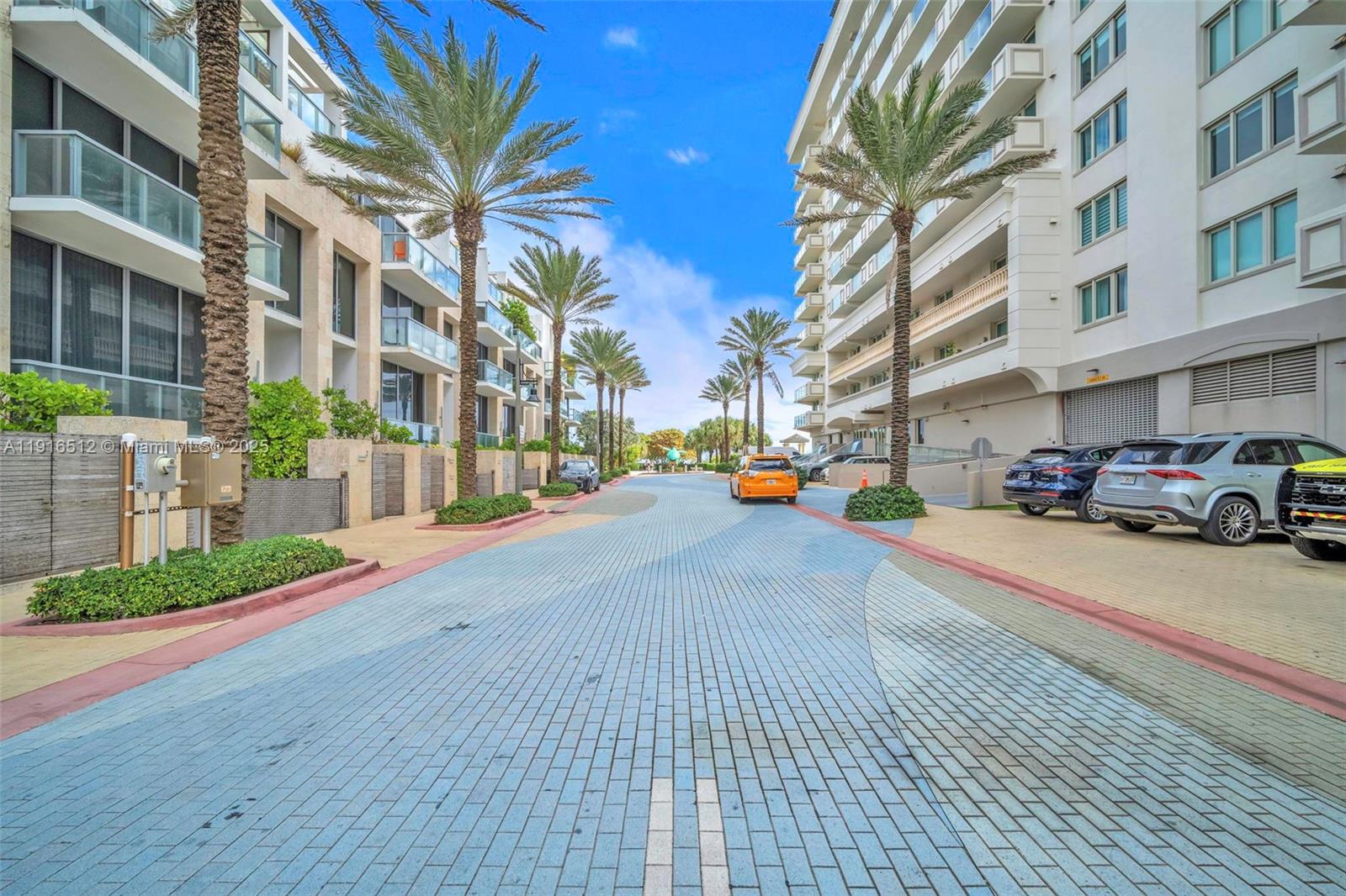 A paved street lined with palm trees runs between two large residential apartment buildings — 9501 Collins Ave # 1, Surfside FL 33154, SURFSIDE, FL