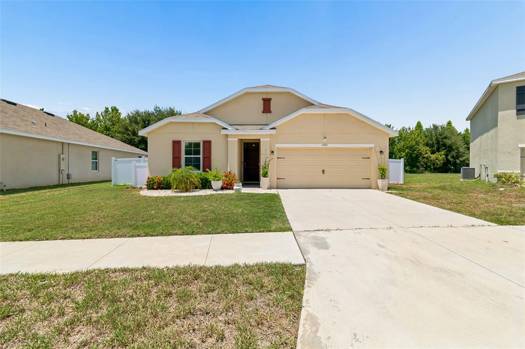 A single-story suburban house with a tan stucco exterior, a two-car garage, and a driveway — 11910 LITTLE VIOLET CIRCLE, RIVERVIEW, FL