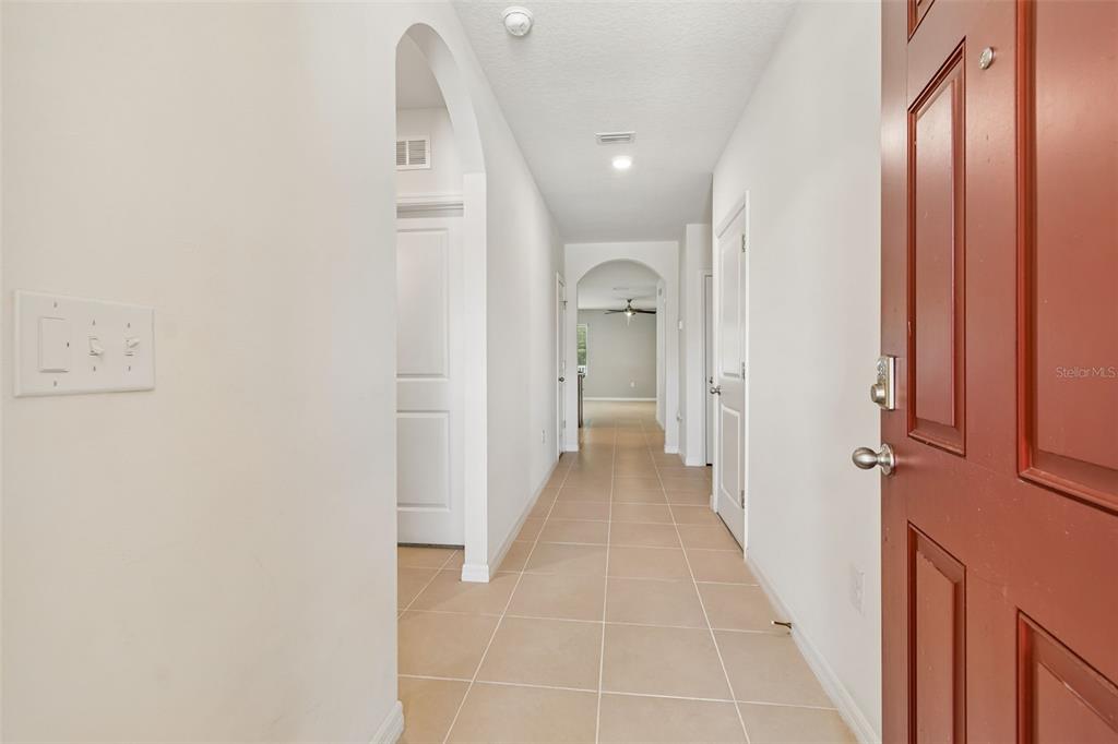 A tiled hallway leads from an open red door toward an arched entryway — 11910 LITTLE VIOLET CIRCLE, RIVERVIEW, FL