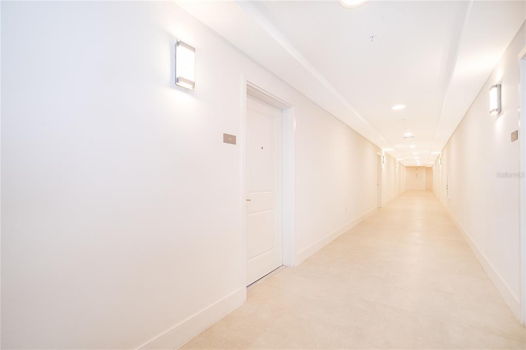 A long, brightly lit apartment hallway features white walls, tiled floors, and closed doors — 5579 MILLENIA PARK BOULEVARD UNIT 219, ORLANDO, FL