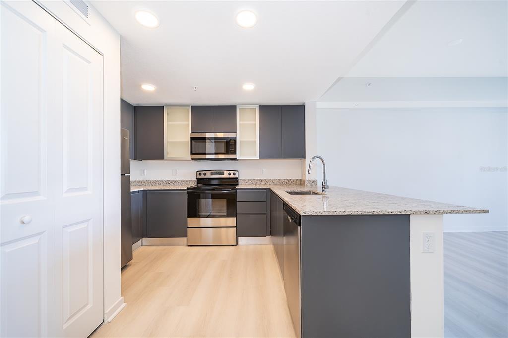 A modern kitchen features dark gray cabinets, stainless steel appliances, and light granite countertops — 5579 MILLENIA PARK BOULEVARD UNIT 219, ORLANDO, FL