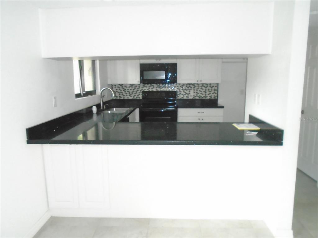 A kitchen features white cabinets, black countertops, a black appliance suite, and a tiled backsplash — 4001 BENEVA ROAD UNIT 349, SARASOTA, FL