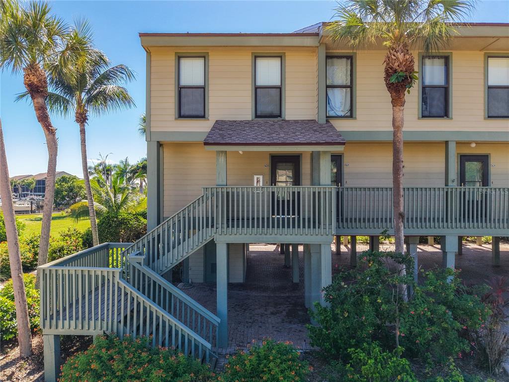 An elevated multi-story building features a wooden staircase leading to a covered front porch — 16750 BOCILLA PALMS DRIVE UNIT 74, BOKEELIA, FL