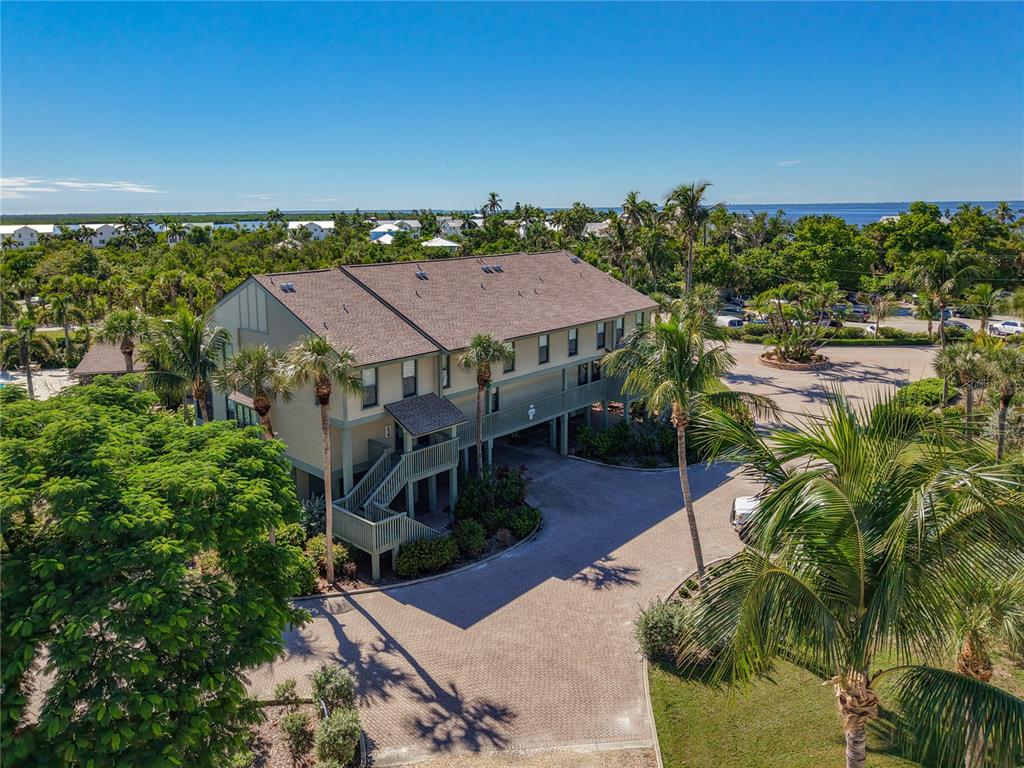 An elevated multi-story building with a shingled roof sits amidst lush tropical landscaping and trees — 16750 BOCILLA PALMS DRIVE UNIT 74, BOKEELIA, FL