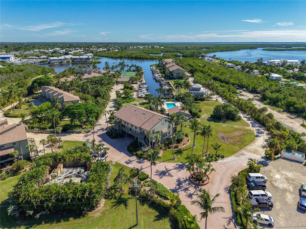 An aerial view shows a multi-story building, a marina with boats, and surrounding tropical landscaping — 16750 BOCILLA PALMS DRIVE UNIT 74, BOKEELIA, FL