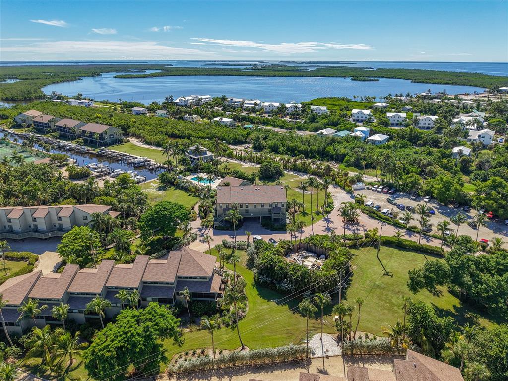An aerial view shows a multi-story residential building surrounded by lush greenery, parking, and water — 16750 BOCILLA PALMS DRIVE UNIT 74, BOKEELIA, FL