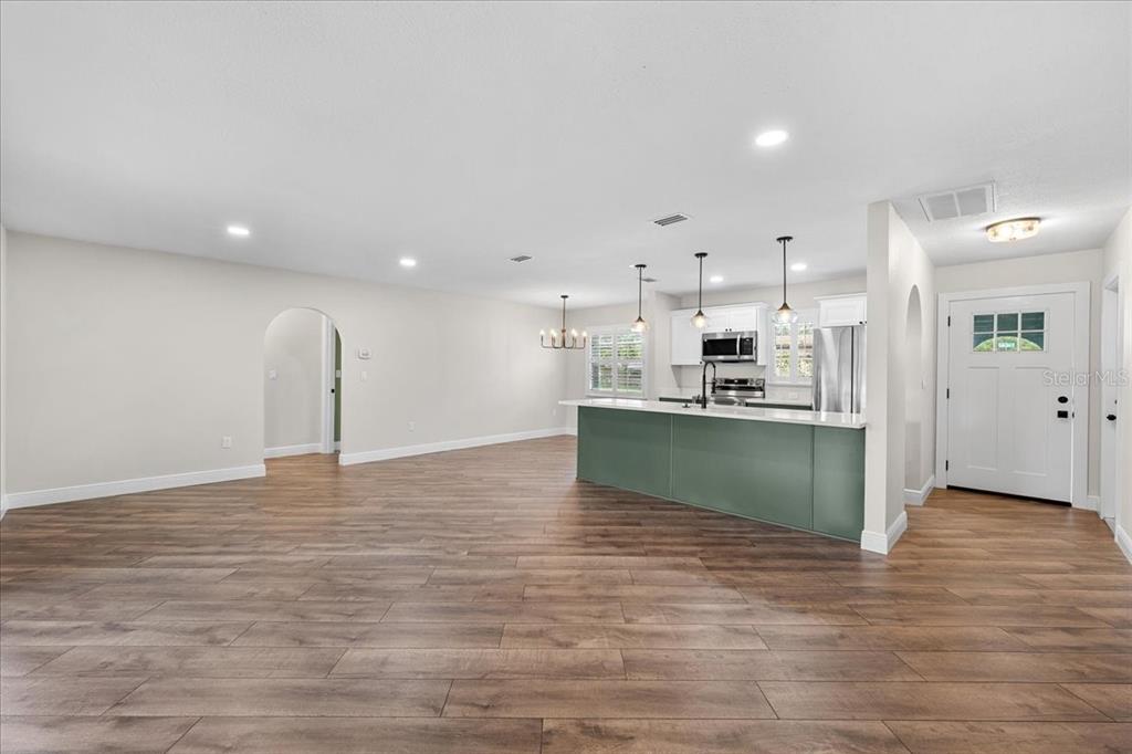 An open-concept kitchen and living area featuring wood-look flooring and a green kitchen island — 12830 LAKE TREE LANE, HUDSON, FL