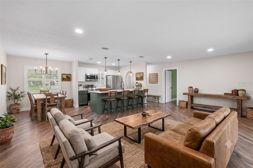 An open-concept living and dining area features a green kitchen island, wood floors, and furniture — 12830 LAKE TREE LANE, HUDSON, FL