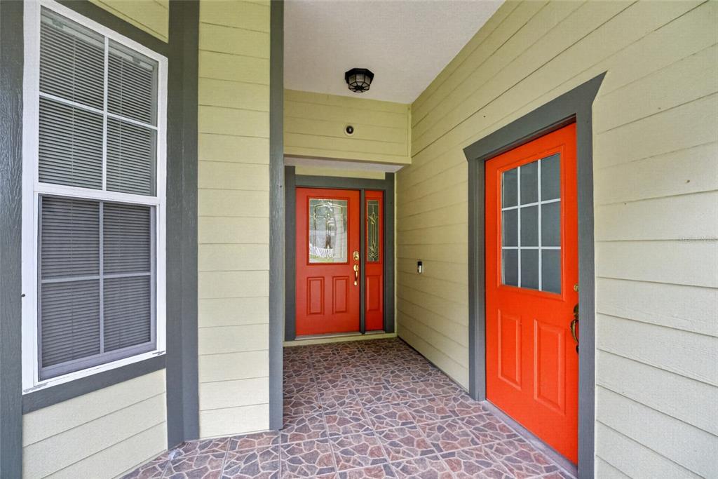 A covered porch features two bright orange doors, light green siding, and patterned tile flooring — 2216 NE 40TH TERRACE, OCALA, FL