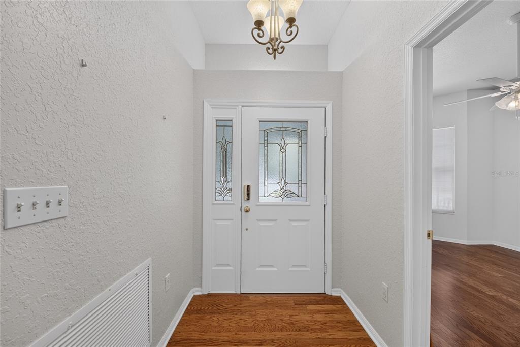 An entryway features a white front door with glass panels, hardwood flooring, and a chandelier — 2216 NE 40TH TERRACE, OCALA, FL